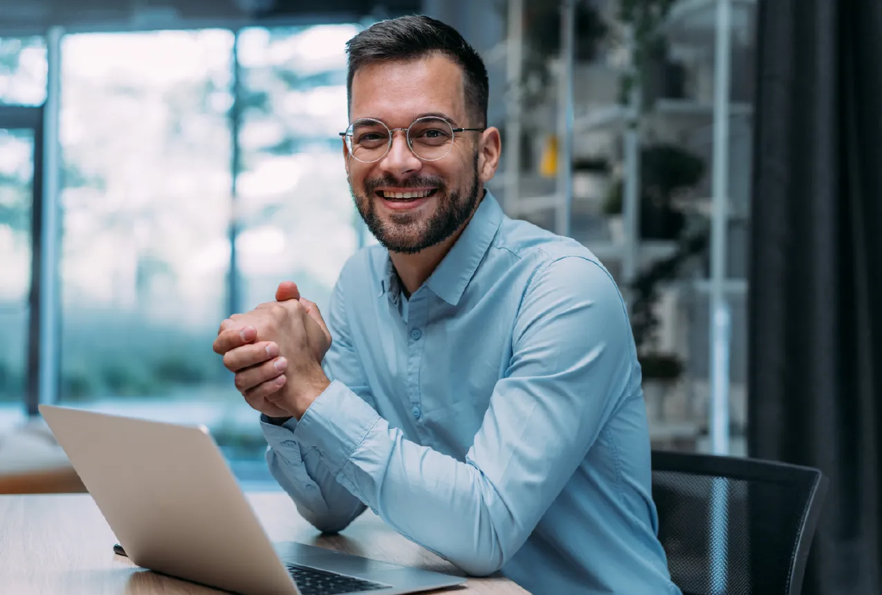 Excited Investor middle aged man with dark hair and glasses clasping his hands and grinning in front of his laptop